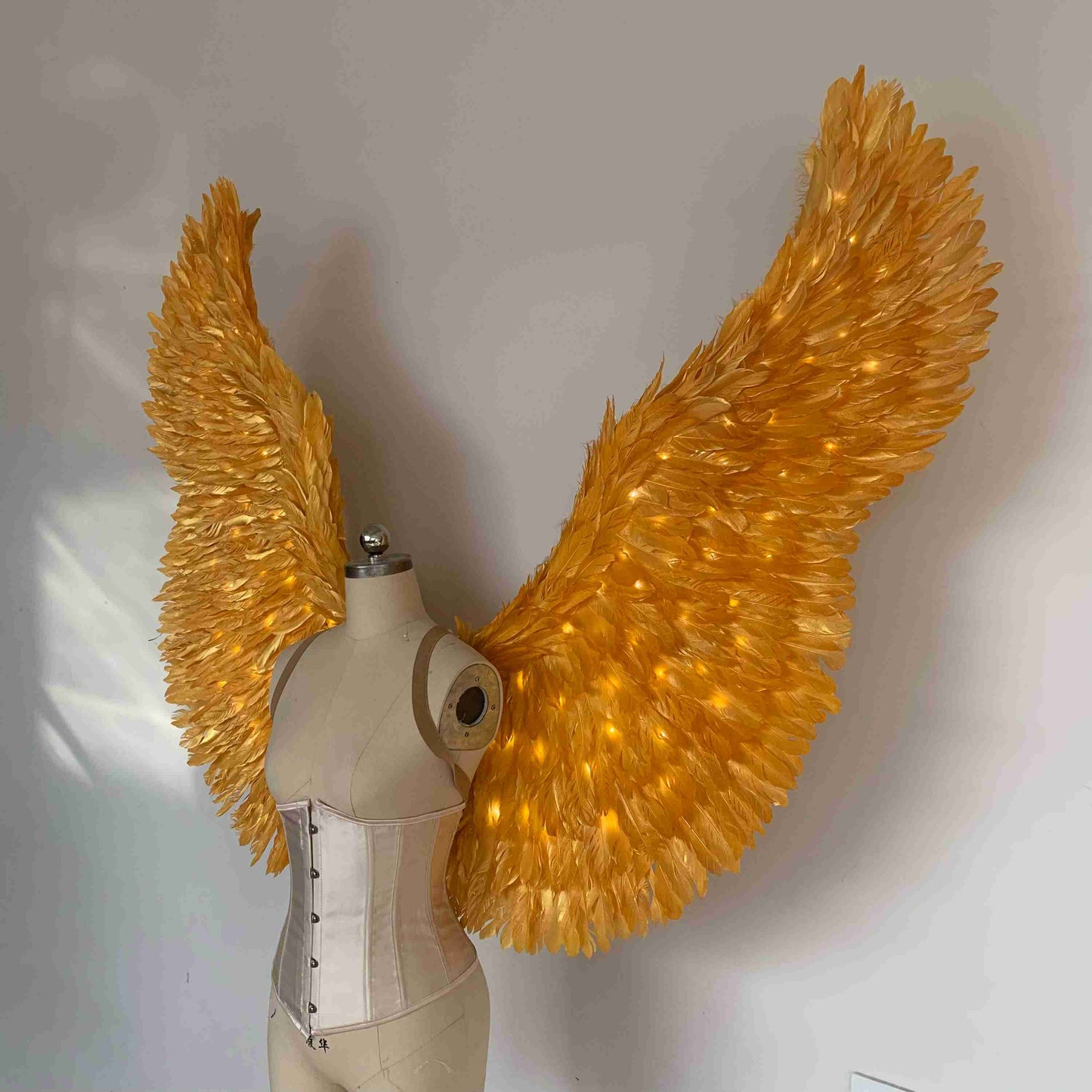 Our gold color angel wings from the left side. Made from goose feathers with LED lights inside. Wings for angel costume. Suitable for photoshoots.